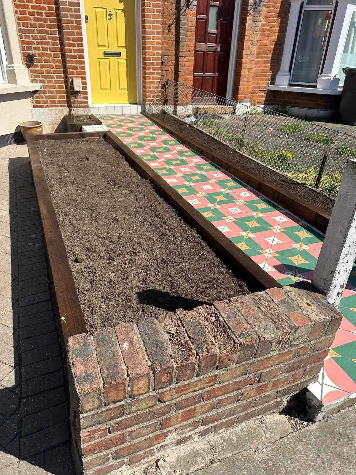 Front garden with brick-faced raised beds and a red and green Victorian tiled path