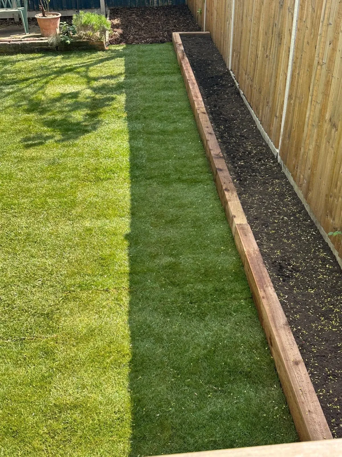 New timber fence along fresh natural turf with a sleeper edge