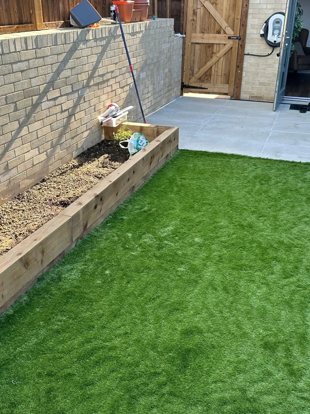 Small back garden rebuilt with an artificial lawn, a timber sleeper raised bed and a grey patio