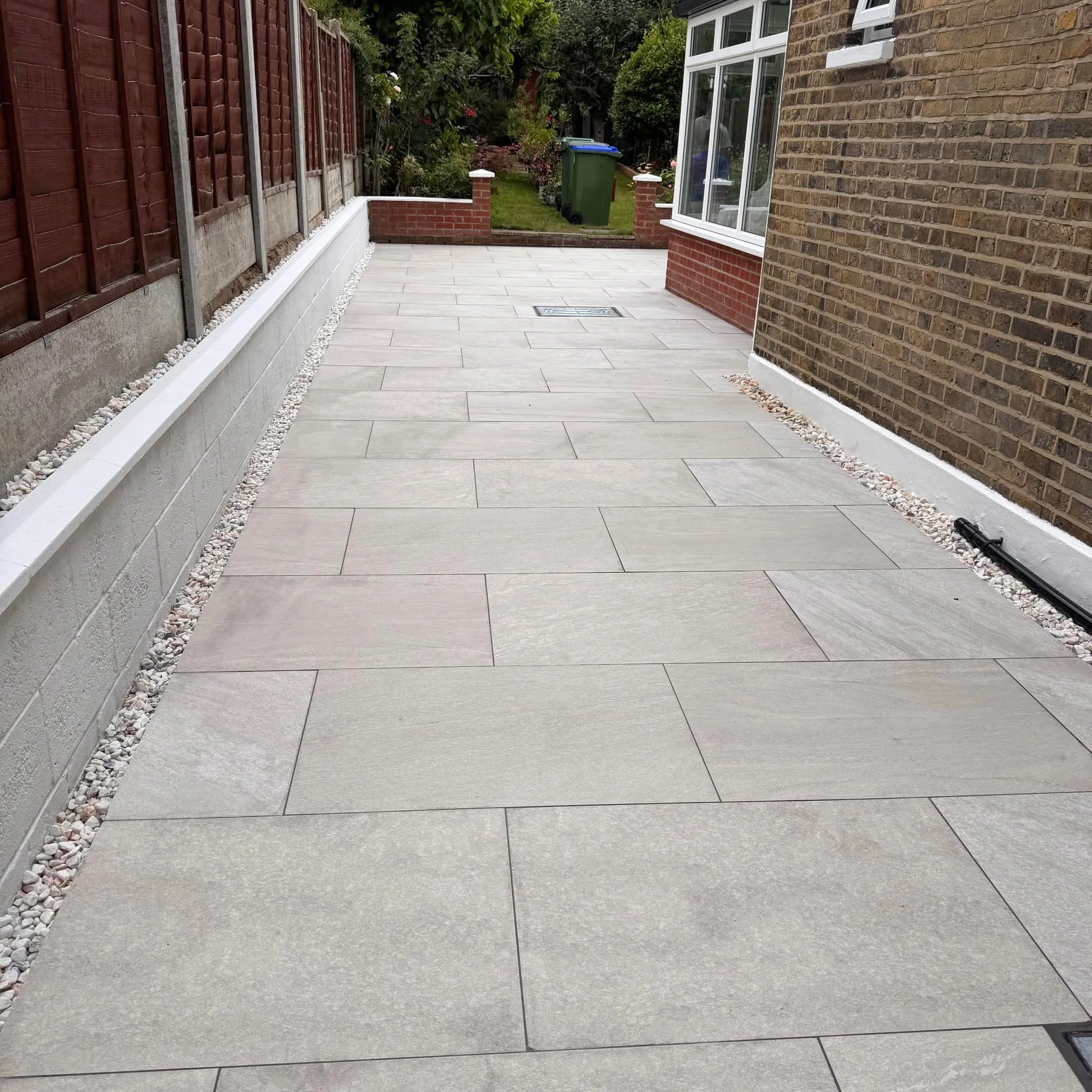 New sandstone-effect paving along the side of a brick house with a rendered wall