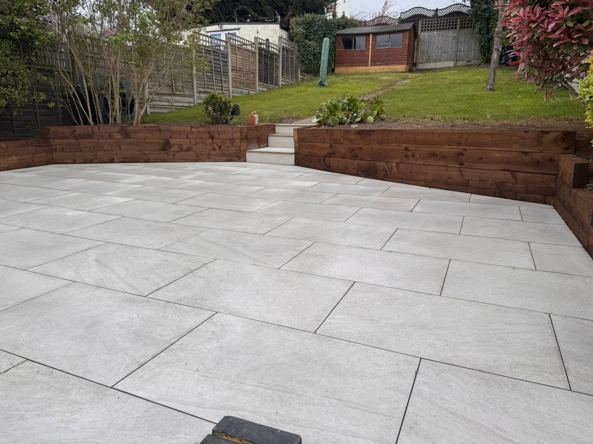 Light grey porcelain terrace with oak sleeper walls and steps up to the lawn