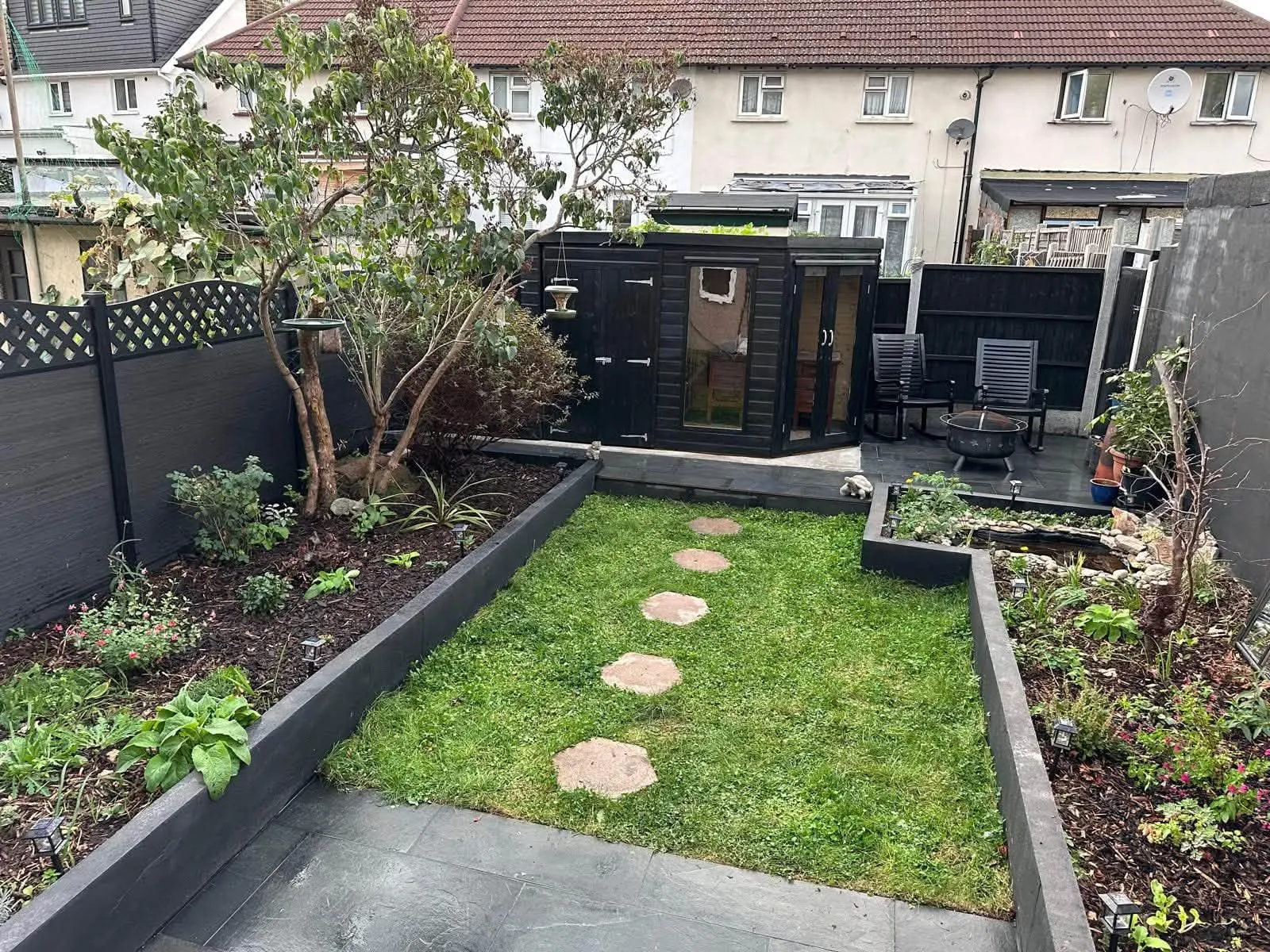 After: lawn with hexagonal stepping stones between black sleeper beds and a garden room