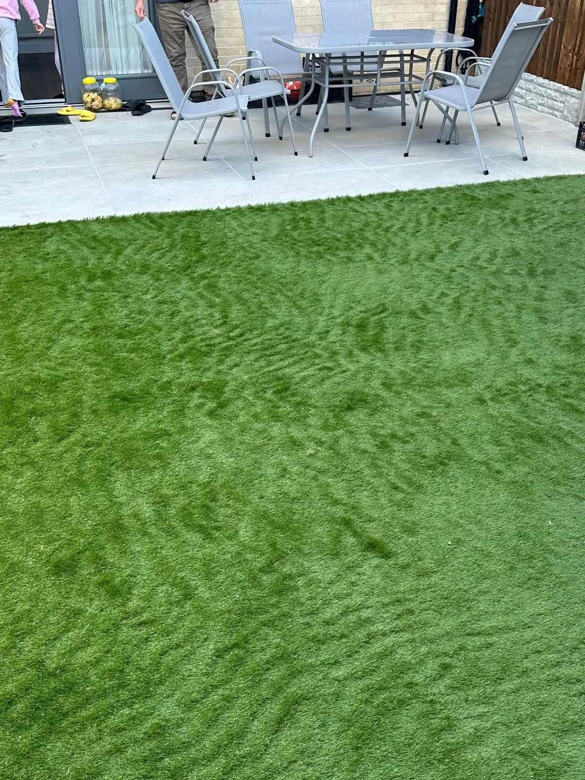 Artificial lawn in front of a grey patio with garden chairs