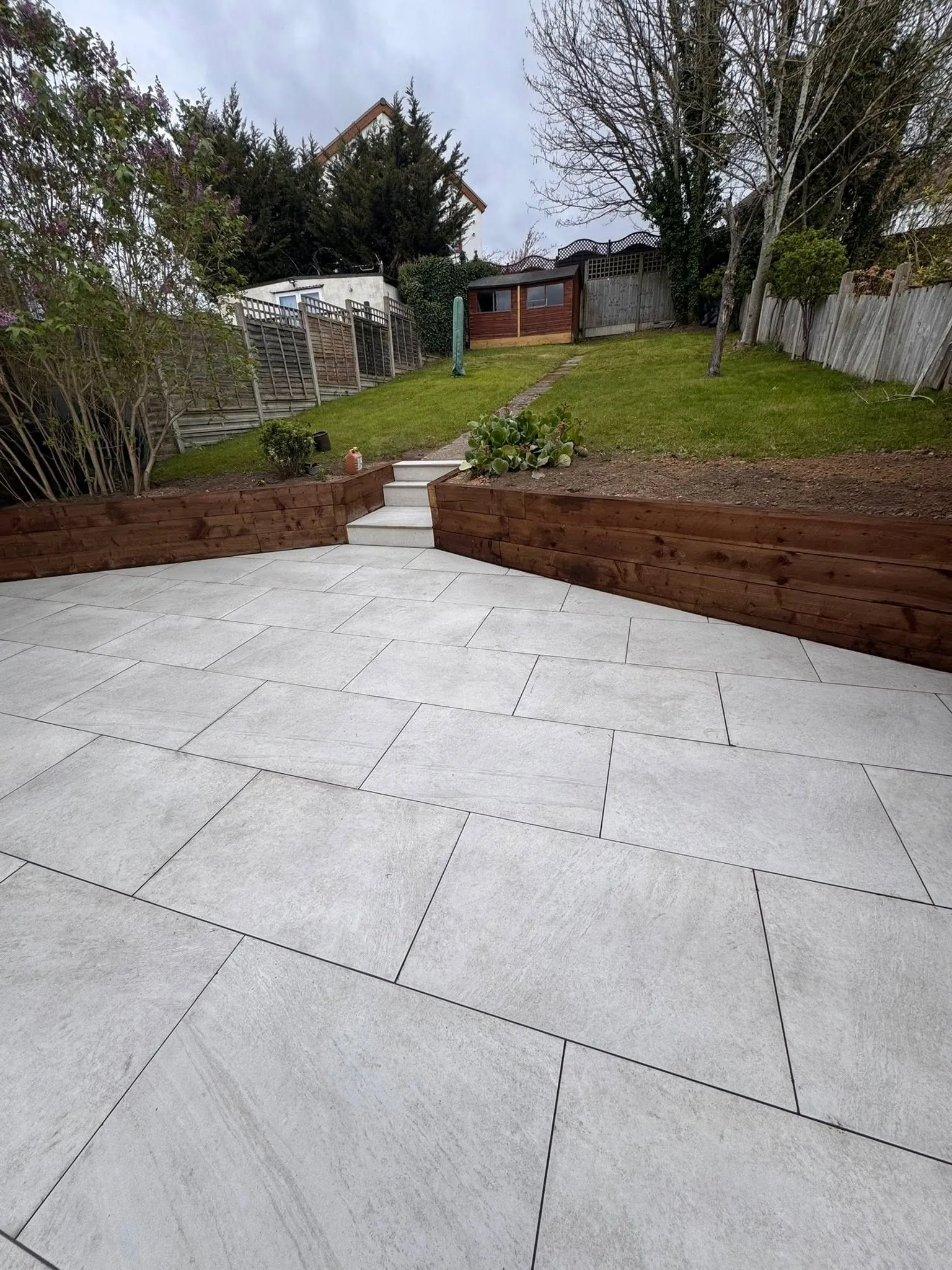 Wide porcelain terrace with oak sleeper walls and a lawn beyond