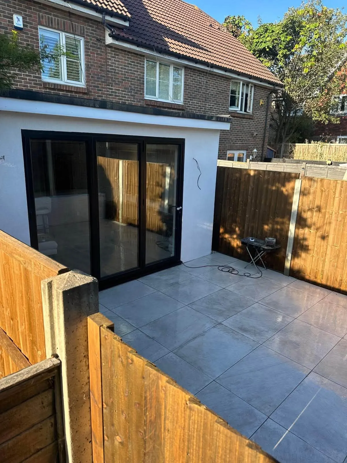 After: new light grey porcelain patio and timber fencing beside a white rendered extension